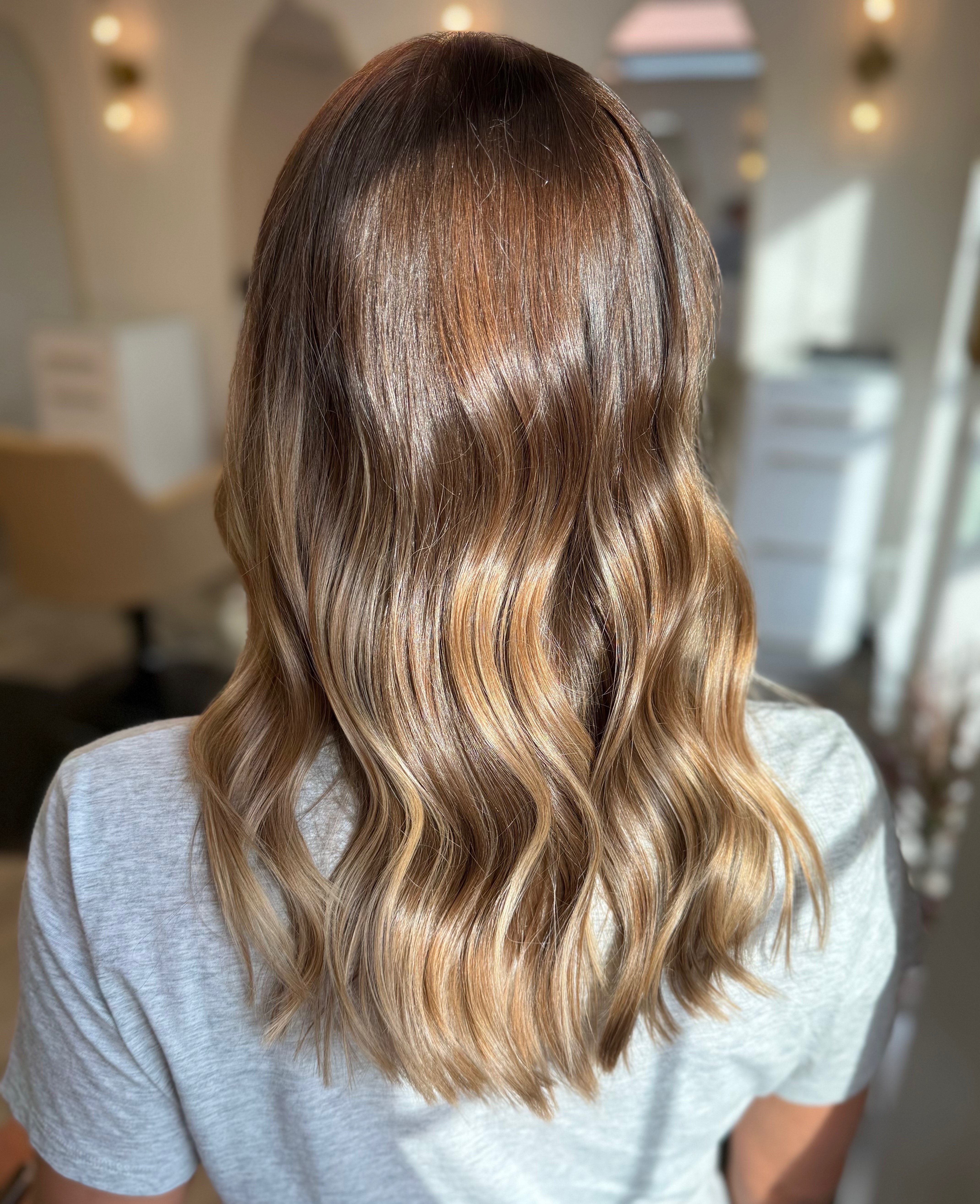 Glossy brunette-to-caramel color melt on long waves by Renovaré